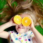Bé gái nằm trên cỏ cười đùa với hai lát cam che trên khuôn mặt