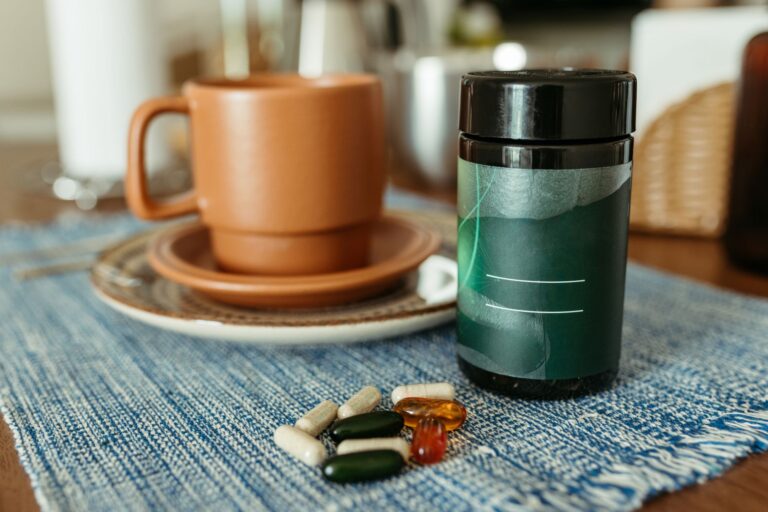 Viên nang thực phẩm chức năng và lọ thuốc xanh đặt cạnh cốc cà phê nâu trên bàn