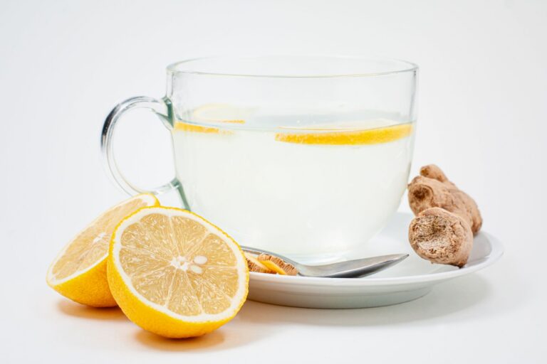 Ly trà nước chanh gừng trong ly thủy tinh với lát chanh và gừng tươi trên nền trắng