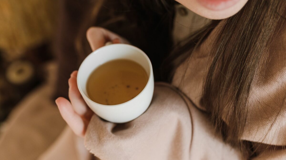 Người phụ nữ mỉm cười cầm chén trà thảo dược màu vàng hổ phách