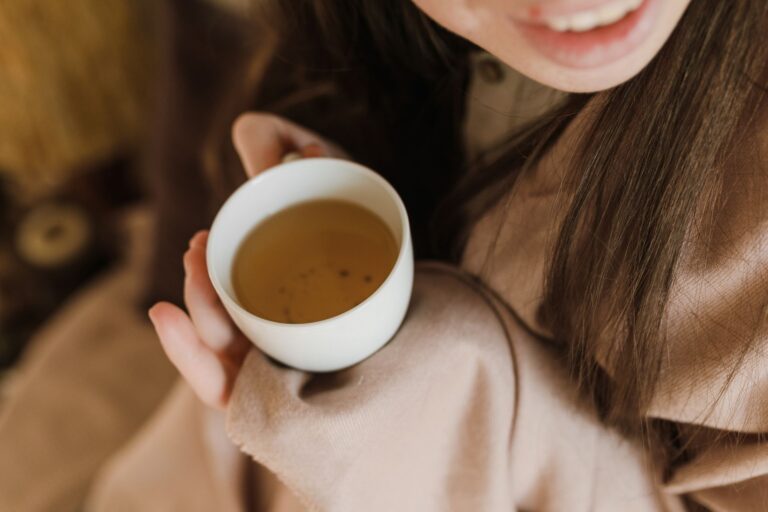 Người phụ nữ mỉm cười cầm chén trà thảo dược màu vàng hổ phách
