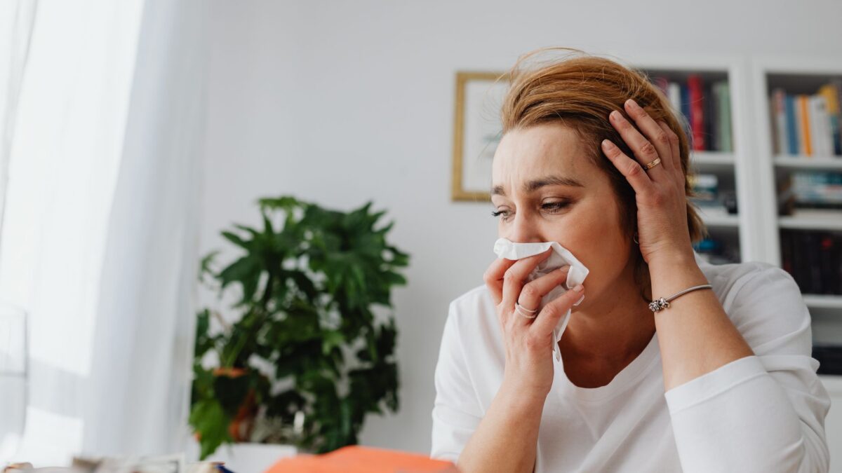 Người phụ nữ đang xì mũi bằng khăn giấy và đặt tay lên đầu vì cảm cúm