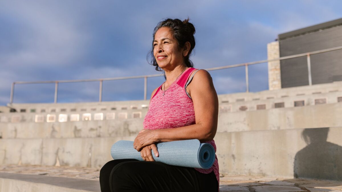 Người phụ nữ trung niên mỉm cười cầm thảm yoga khi đi bộ ngoài trời