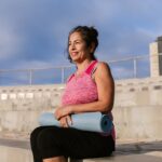 Người phụ nữ trung niên mỉm cười cầm thảm yoga khi đi bộ ngoài trời