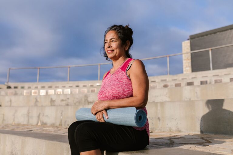 Người phụ nữ trung niên mỉm cười cầm thảm yoga khi đi bộ ngoài trời